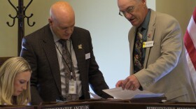 Three people look at papers next to an American flag.