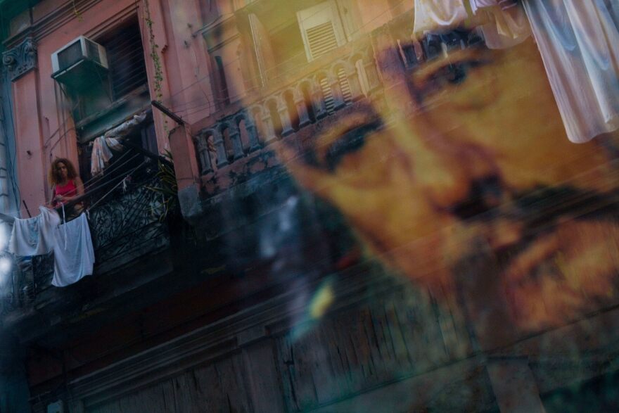 FILE - A Cuban woman hanging laundry on her balcony is seen reflected in a glass window decorated with a poster of Cuba's leader Fidel Castro in Old Havana, Cuba, Thursday, Dec. 27, 2007.