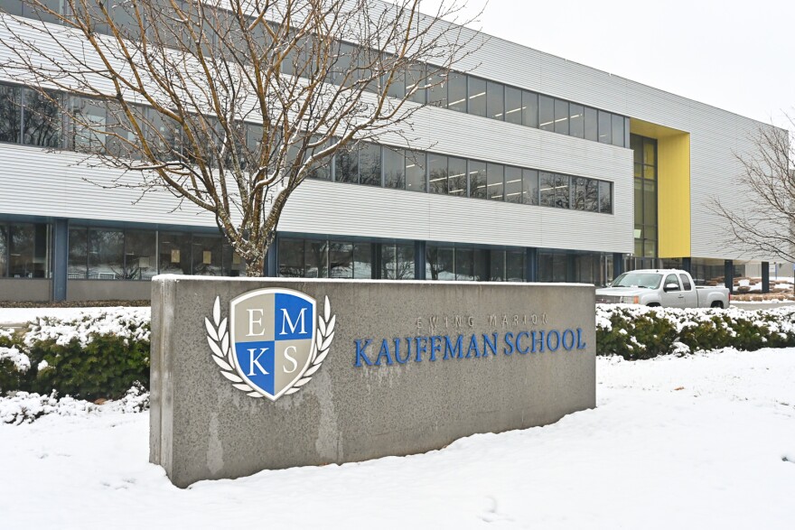 A large concrete rectangle sits in the snow in front of a modern, three-story building with lots of windows. The concrete block is a sign in front of the school. It reads "Ewing Marion Kauffman School."