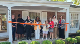 people stand on house porch and cut an orange ribbon with comically large scissors