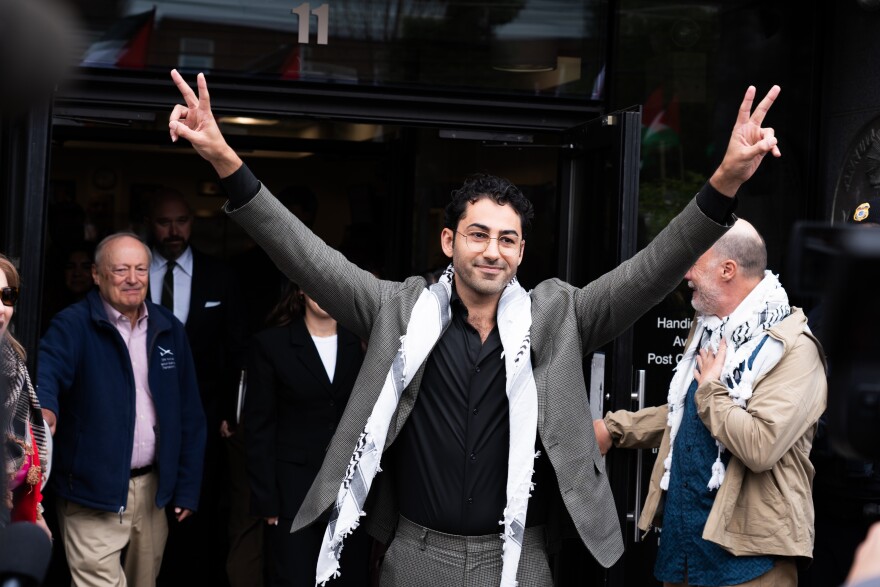 A man holds up peace signs while walking out of a court building