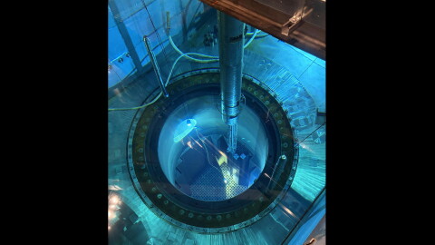 The image is shot from above a pool of blue water. A circular hole sits inside, just below other parts of the submerged metal. A silver metal rod can be seen above the water holding a smaller metal rod that is partially submerged. Various pipes and tubes also feed in and out of the pool. 