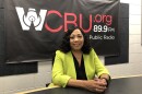 Peoria Mayor Rita Ali sits at a table in the WCBU newsroom studio with the station's banner in the background.  