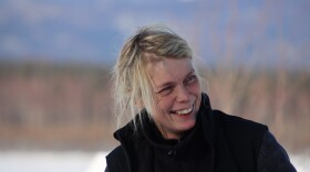 A blond woman smiles in front of some trees