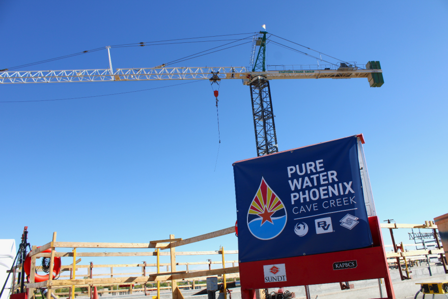 Cranes looming over a construction site. There's a sign in front that says "Pure Water Phoenix, Cave Creek" with the project's symbol and symbols for collaborators or funders.
