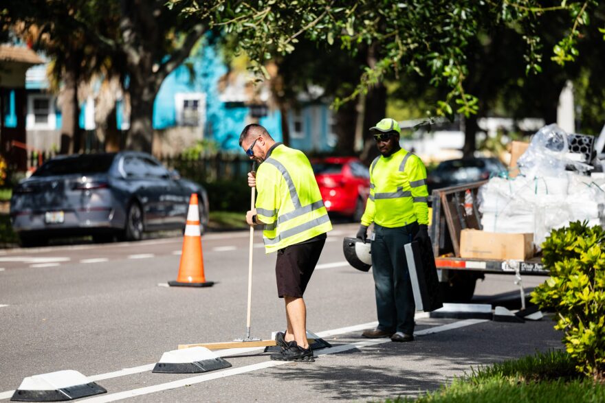 Workers install barrier devices between road and bike lane