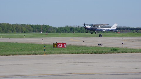 A student pilot in a small blue and white airplane practices touch and go landings and takeoffs at Kalamazoo Battle Creek International Airport in front of a red and white mandatory instruction sign.