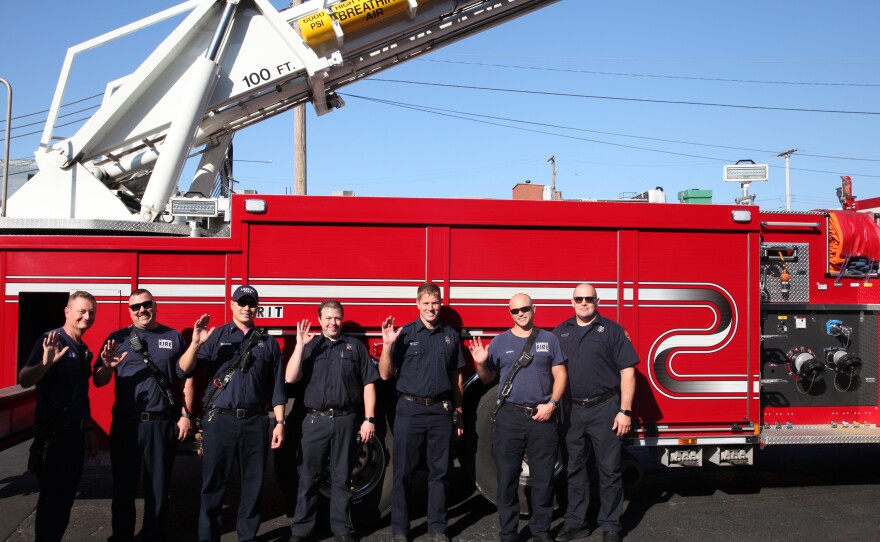 Members of the Lansing Fire Department pose with a fire truck in front of Impression 5 Science Center.
