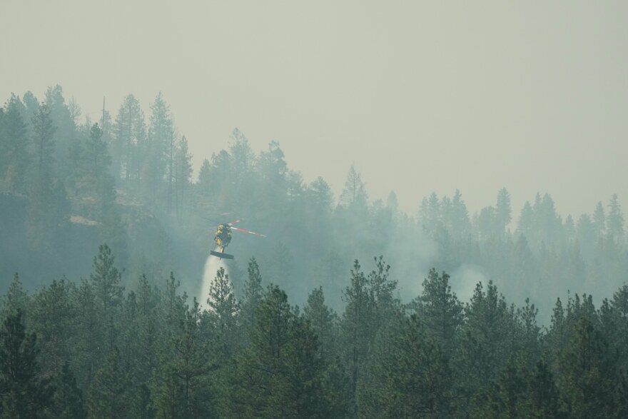 A firefighting helicopter dumps water on a wildfire in the northwest part of Spokane, Wash., Tuesday, Aug. 4, 2026. (AP Photo/Lindsey Wasson)