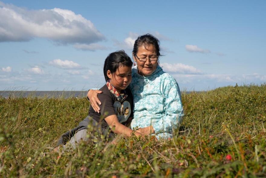 Lena Ayuluk and her grandmother, Albertina Charles, sit surrounded by berries and Labrador tea behind Charles' home in Mertarvik, Alaska. (Katie Basile/KYUK)