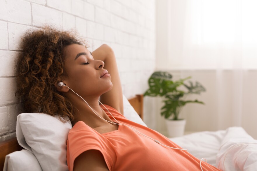 A woman with headphones on relaxes while listening to music.