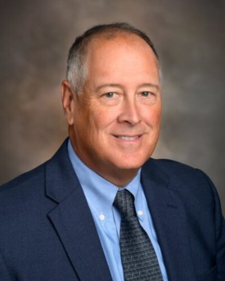 Headshot of a man with a blue shirt and suit jacket