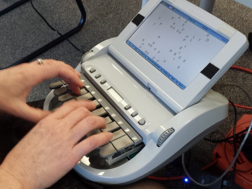 Hands typing on a stenographer keyboard screen.