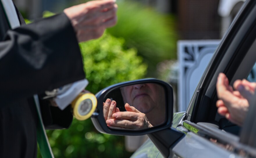 Rev. Paul Fagan gives parishioners in vehicles communion and blesses them with a relic during St. Ann's solemn Novena.