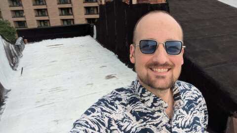 Owen Henry, standing on the roof of his Baltimore rowhome, painted his roof white in 2023 so he could help cool the home and save on energy costs. It worked, he says, reducing electricity use by 24%.
