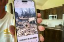 Pine Valley resident Dale Hagemeyer holds up a photo of his home’s charred remains after it was destroyed by the Forsyth Fire. Over the past year, he and his wife have been working to build a new house, seen here, May 20, 2026, in that same spot.