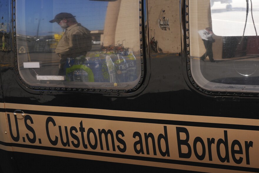 A U.S. Customs and Border Protection agent walking past is reflected in the window of a helicopter at Homestead Air Force Base 