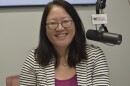 State Rep. Sharon Chung in a radio studio in a black-and-white striped suit jacket seated next to a microphone with the mic flag labeled 'WGLT.org 89.1 FM'