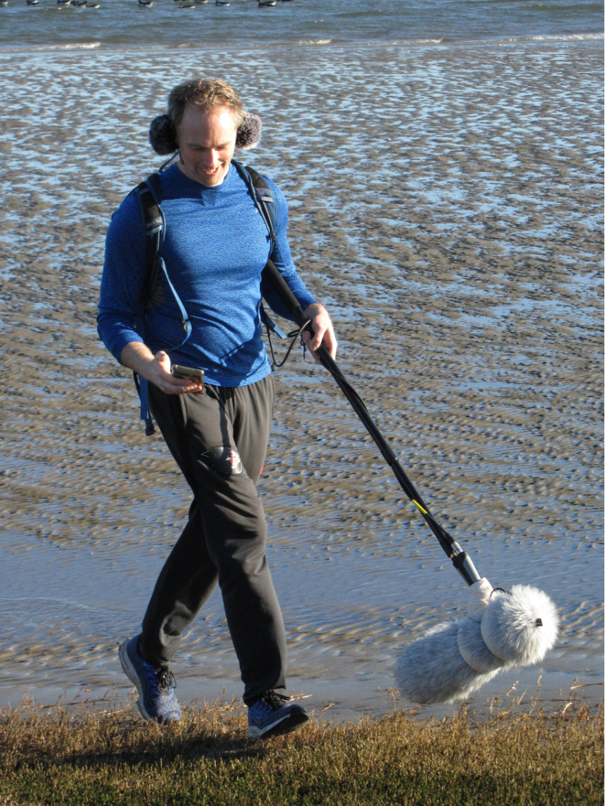 Chet Udell looks at his flashing metronome as he carries a boom microphone recording his footfalls and other environmental sound while he jogged around Newport, Ore., on Jan. 19, 2026.