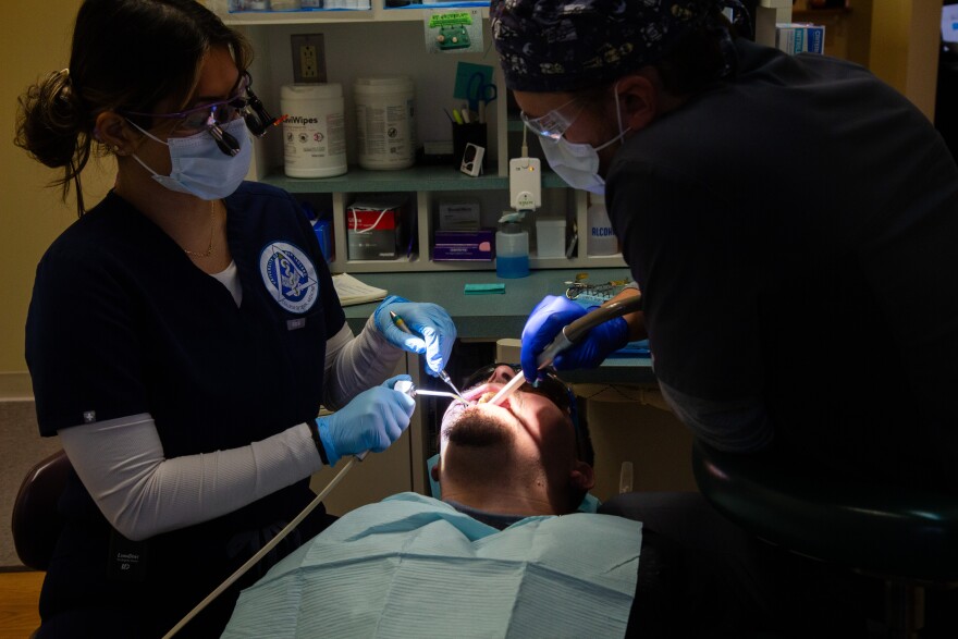 A photo of two dental workers holding tools in a patient's mouth.