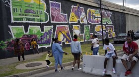 People walk by a mural for Black Wall Street in the Greenwood district during centennial commemorations of the Tulsa Race Massacre, Sunday, May 30, 2021, in Tulsa, Okla.