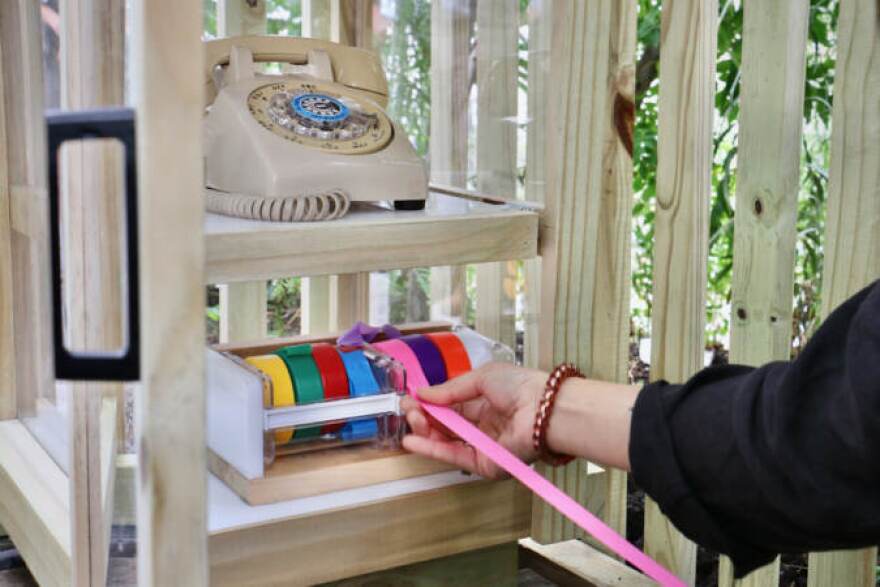 Visitors are encouraged to write a name of or a message to a loved one who has died on the colorful ribbon provided in the phone cabinet, then tie the ribbon to the fence along the Rail Park walkway.