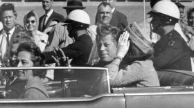 President John F. Kennedy waves from his car in a motorcade approximately one minute before he was shot, Nov. 22, 1963, in Dallas. Riding with President Kennedy are first lady Jacqueline Kennedy, right, Nellie Connally, second from left, and her husband, Texas Gov. John Connally, far left.
