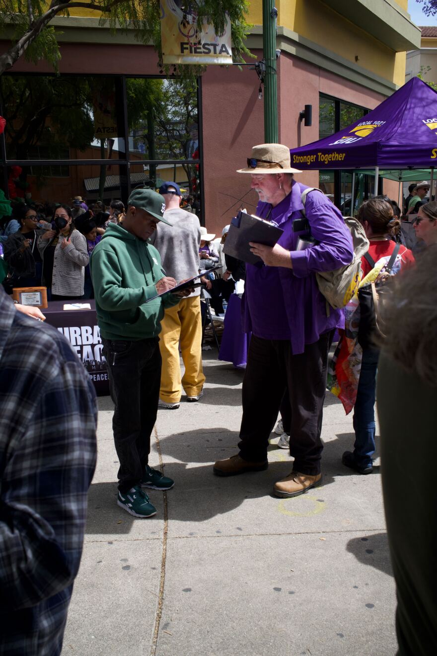 Jason Gordon (left) of Oakland discusses a ballot measure with petitioner Jim Ray of Vallejo at the Fruitvale Village May Day rally in Oakland. Ray is canvassing voters to help support a sales tax that would fund transit around the Bay Area.