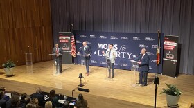 four men stand at podiums on a stage