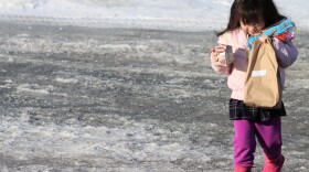 Meena Yang, 4, carries breakfast and lunch from the school bus in Glencaren Court in East Anchorage on Friday, March, 20, 2020. The Anchorage School District is distributing free meals to students while schools are closed due to coronavirus. (Tegan Hanlon/Alaska Public Media)