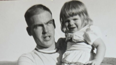 Black and white photo of smiling young girl in a white dress, held by young man looking pensive