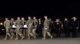 Soldiers carry coffin on tarmac while president solutes.