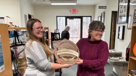 Two women smile and hold a wooden award.