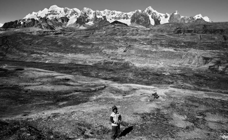 A snow-covered Andean peak near the Interoceanic Highway's highest point outside Ocongate looms over a young Quechua llama herder. The highway is having a profound impact on migration, bringing an estimated 200 to 300 people daily from the Andean highlands to the Amazon Basin, most of whom will work in the mining sector.