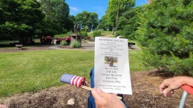  hand holds program with memorial in background