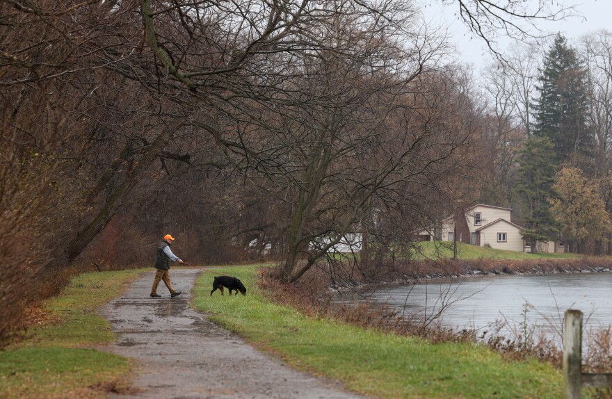 A man walks a black dog next to the canal