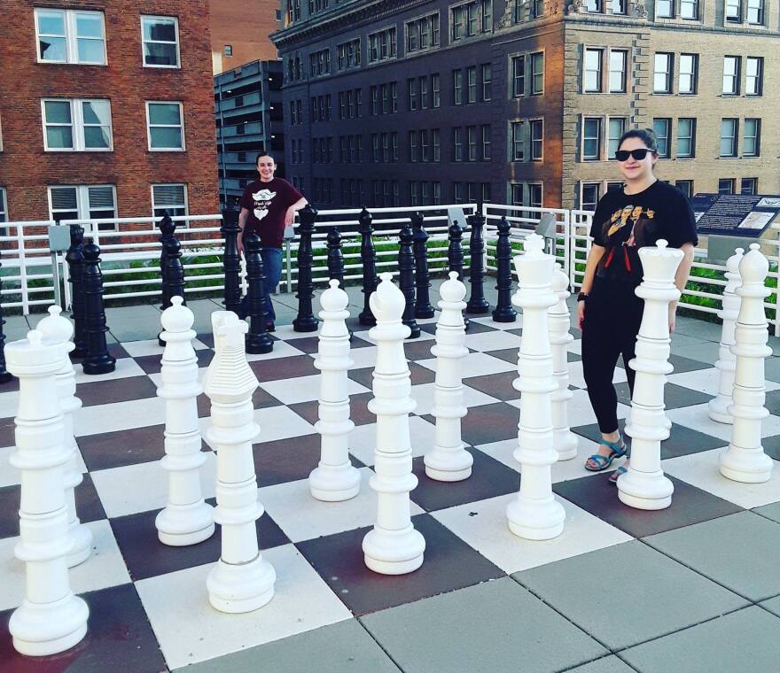 Two women stand with the giant chess set on the rooftop patio of the Kansas City Public Library.