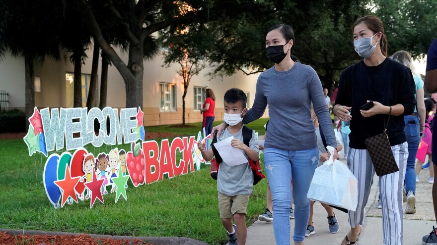 Parents and relatives wearing protective masks walk children to class before the first day of school at Sessums Elementary School Tuesday, Aug. 10, 2021, in Riverview, Fla.