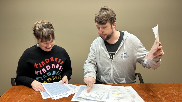 Two people looking at papers on a wood table wearing a black sweatshirt and gray hoodie.