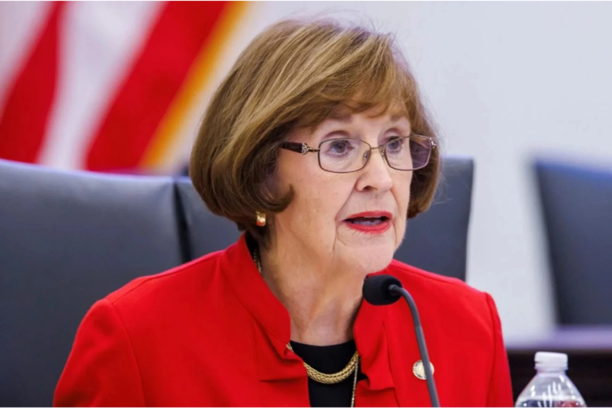 Una mujer de pelo rubio corto y gafas, sentada junto a un micrófono. Lleva puesta una chaqueta roja.