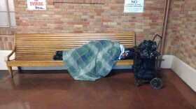 A homeless person sleeps on a wooden bench inside San Jose's Diridon station.