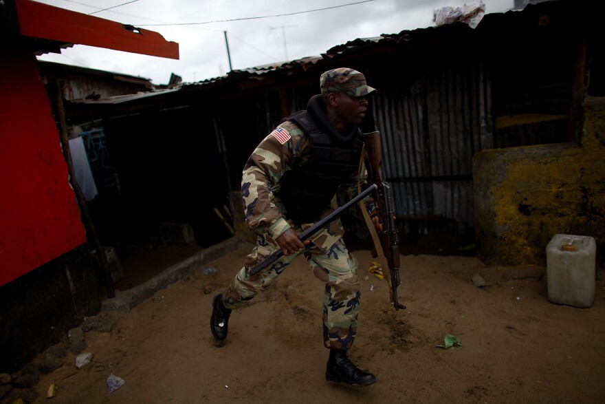 A soldier chases protesters through West Point after Liberia enforced a quarantine of the area.