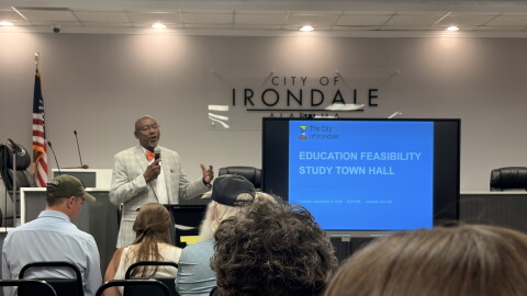 Irondale Mayor James Stewart speaks to an audience and stands beside a screen that reads "Education Feasibility Study Town Hall."