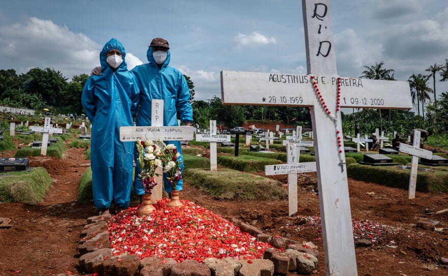 Two men, wearing personal protective equipment, visit the grave of a relative at Pondok Rangon public cemetery, reserved for suspected COVID-19 victims, on Dec. 24, 2020 in Jakarta, Indonesia.