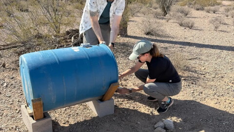 Volunteers for Humane Borders refill a water barrel in the desert.