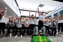 group of college age women, all in gray T-shirts sitting, leap in the air in celebration 