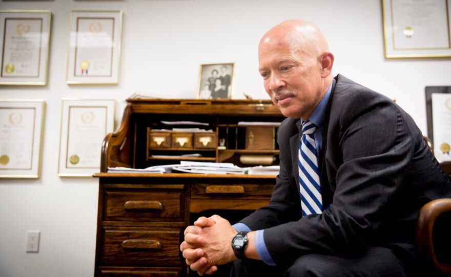 Dallas County District Attorney John Creuzot sits in a chair in his private law office. His elbows are on his knees. He's slumped over and looking down. Creuzot holding his hands together.
