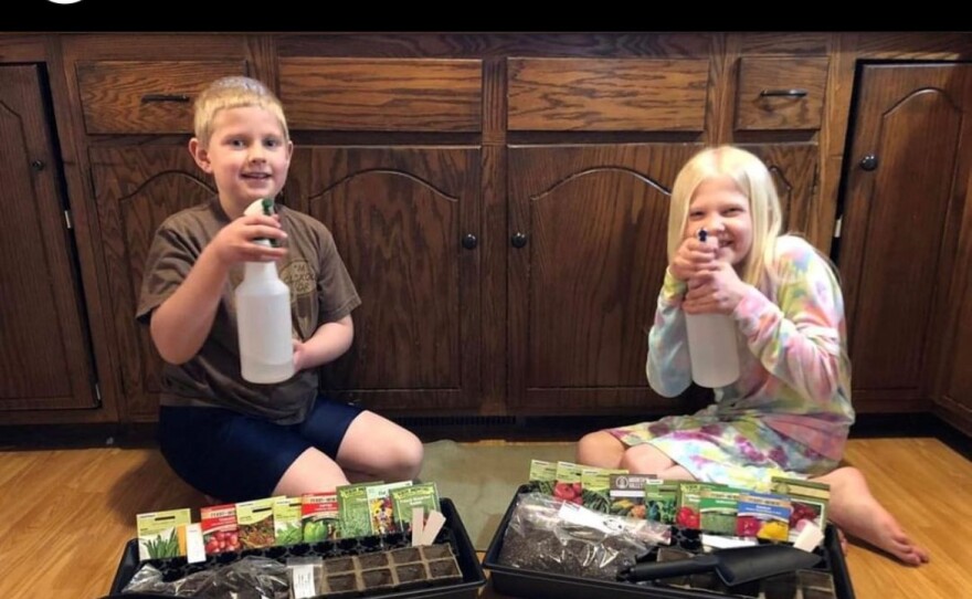 Two children sit happily with their gardening grow kits, pointing their water bottles at the camera as if to spray the viewer