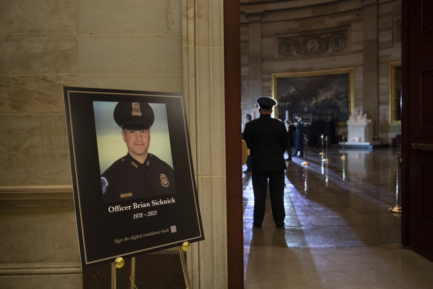 In this Feb. 2, 2021, file photo a placard is displayed with an image of the late U.S. Capitol Police officer Brian Sicknick on it as people wait for an urn with his cremated remains to be carried into the U.S. Capitol to lie in honor in the Capitol Rotunda in Washington. 