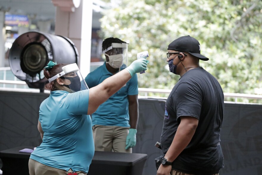 FILE—In this June 3, 2020 file photo, a Universal Studios employee takes the temperature of a guest entering the theme park in Orlando, Fla. Amusement parks of all sizes are adjusting everything from selling tickets to serving meals while trying to reassure the public and government leaders that they're safe to visit amid the coronavirus crisis and warnings against large gatherings. (AP Photo/John Raoux, File)